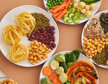 A vibrant mix of legumes, vegetables, nuts, and pasta arranged on white plates showcasing a balanced, healthy diet.